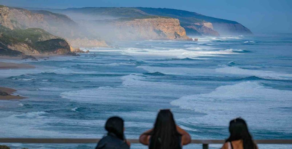 3 girls looking out at Great ocean road wild coastline and stormy waves due to wind